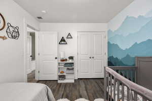 Bedroom featuring a nursery area, a closet, and dark wood-style floors