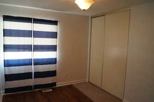 Unfurnished bedroom with dark wood-style floors and a closet