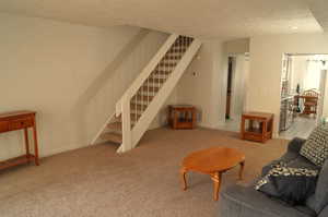 Living area with stairway, a textured ceiling, and light colored carpet