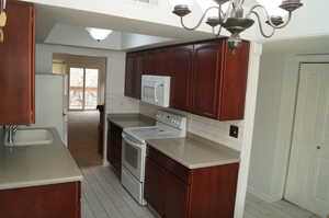 Kitchen with hanging light fixtures, white appliances, dark brown cabinets, and tasteful backsplash