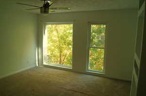 Carpeted master bedroom featuring a textured ceiling and ceiling fan