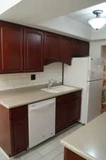 Kitchen with dark brown cabinets, light countertops, white appliances, and tasteful backsplash