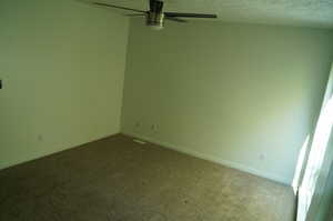 Empty room featuring carpet floors, a textured ceiling, and a ceiling fan