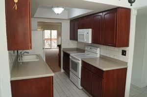 Kitchen featuring dark brown cabinets, white appliances, decorative backsplash, and a raised ceiling