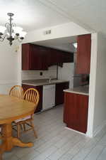 Kitchen featuring hanging light fixtures, white appliances, reddish brown cabinets, tasteful backsplash, and a chandelier