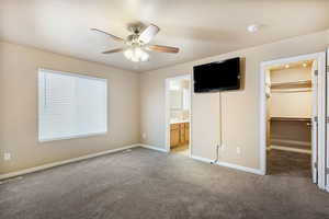 Unfurnished bedroom with a spacious closet, light carpet, ceiling fan, and connected bathroom