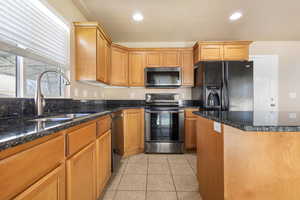 Kitchen with stainless steel appliances, dark stone counters, recessed lighting, light tile patterned floors, and brown cabinetry