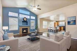 Living area featuring a tiled fireplace, ceiling fan, light wood-style floors, high vaulted ceiling, and a chandelier