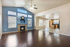 Unfurnished living room featuring dark wood-style floors, a tile fireplace, a ceiling fan, a chandelier, and high vaulted ceiling