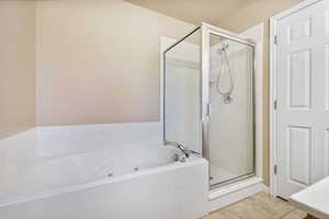 Bathroom featuring a stall shower, a jetted tub, and light tile patterned flooring
