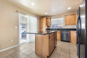 Kitchen with freestanding refrigerator, a center island, dishwasher, light tile patterned flooring, and recessed lighting