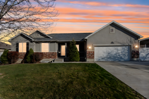 View of front of property with brick siding, driveway, a front yard, stucco siding, and a garage