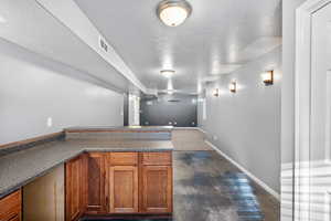Bar with brown cabinets, a textured ceiling, finished concrete floors, and dark countertops
