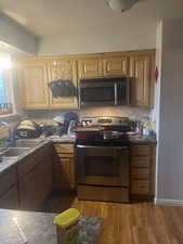 Kitchen with appliances with stainless steel finishes, light wood finished floors, dark countertops, tasteful backsplash, and brown cabinetry