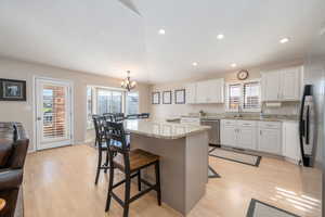 Kitchen featuring white cabinets, hanging light fixtures, a center island, a kitchen breakfast bar, and light stone counters