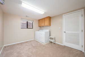 Laundry room featuring cabinet space, washer and clothes dryer, light carpet, and a textured ceiling