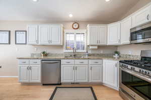 Kitchen with stainless steel appliances, white cabinetry, light wood-type flooring, light stone counters, and a textured ceiling