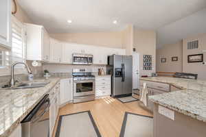 Kitchen with appliances with stainless steel finishes, light wood-style flooring, light stone counters, white cabinetry, and high vaulted ceiling
