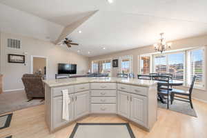 Kitchen featuring gray cabinetry, a center island, vaulted ceiling, pendant lighting, and light wood-type flooring