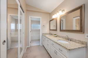 Full bathroom with vaulted ceiling, double vanity, light colored carpet, and a tub to relax in