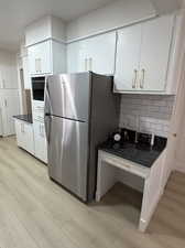Kitchen with white cabinetry,& brushed gold finishes, New  freestanding refrigerator, light wood laminate flooring, and decorative backsplash