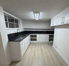 Kitchen featuring tasteful granite countertops, double basin stainless steel sink with light wood-style floors, white cabinetry, brushed gold handles.
