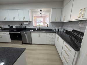 Kitchen featuring new stainless steel appliances, white cabinetry with brushed gold hardware, dark stone countertops, subway tile backsplash, and stunning ight wood laminate floors