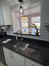 Kitchen featuring subway tile backsplash, white cabinets with brushed gold finishes, gorgeous granite countertops, and decorative hanging  light fixtures