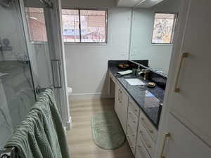 Full bathroom featuring Euro glass sliding shower door, white vanity with brushed gold finishes, , beautiful granite countertops, light wood finished floors, and plenty of natural light