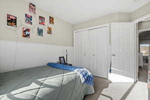 Carpeted bedroom featuring a closet and a wainscoted wall