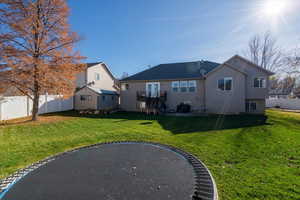Back of house featuring a trampoline, a fenced backyard, a patio, and a wooden deck