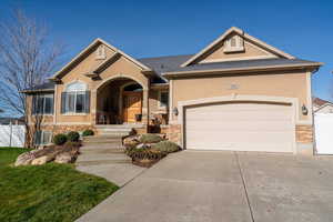 View of front of property with stone siding, concrete driveway, and stucco siding