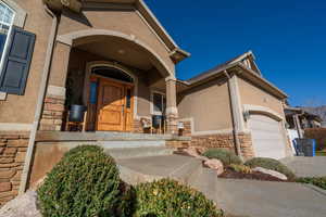 Property entrance with stone siding, covered porch, stucco siding, and a garage