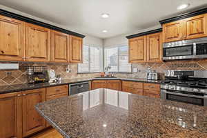 Kitchen featuring stainless steel appliances, brown cabinets, dark stone counters, recessed lighting, and decorative backsplash