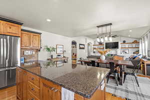 Kitchen featuring recessed lighting, freestanding refrigerator, lofted ceiling, brown cabinetry, and dark stone countertops