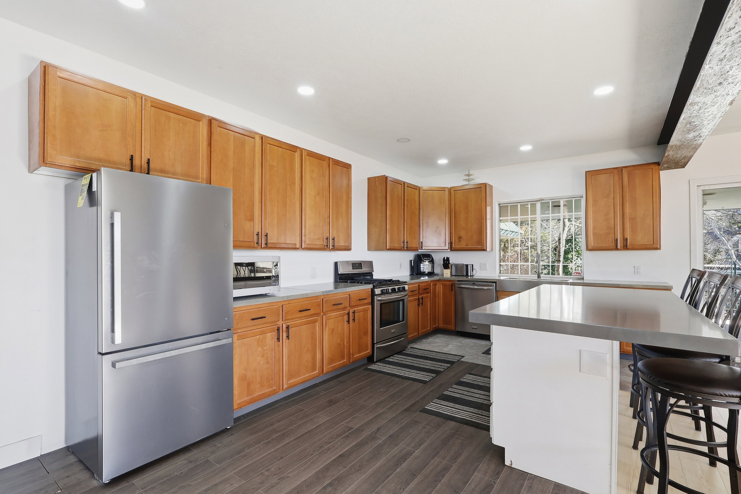 Kitchen with a kitchen bar, appliances with stainless steel finishes, dark wood-style flooring, recessed lighting, and brown cabinets