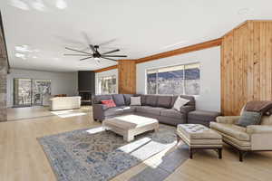 Living area featuring ceiling fan, wood walls, light wood-style floors, and ornamental molding