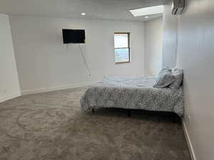 Bedroom featuring a textured ceiling, carpet, a skylight, recessed lighting, and an AC wall unit