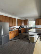 Kitchen featuring brown cabinets, stainless steel appliances, a kitchen breakfast bar, dark wood-type flooring, and a textured ceiling