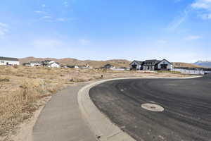 View of asphalt road featuring a mountain view, curbs, and sidewalks