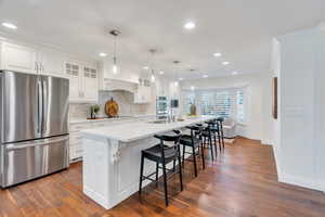 Kitchen featuring glass insert cabinets, black appliances, a kitchen bar, white cabinets, and a large island