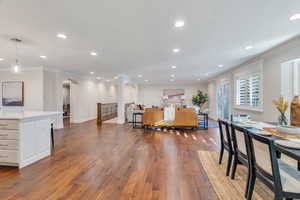 Living area with dark wood-style flooring, ornamental molding, recessed lighting, arched walkways, and ornate columns