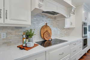 Kitchen with custom range hood, white cabinetry, light stone countertops, stainless steel double oven, and black electric stovetop
