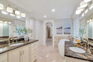 Full bath with two vanities, crown molding, a soaking tub, a walk in closet, and recessed lighting