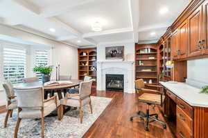 Dining area featuring coffered ceiling, built in study area, beamed ceiling, dark wood-style flooring, and a fireplace