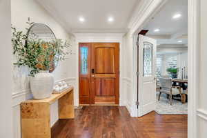 Foyer entrance with wainscoting, a decorative wall, crown molding, and dark wood finished floors