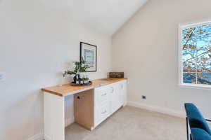 Office space featuring light colored carpet and lofted ceiling