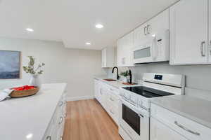 Kitchen with white appliances, white cabinets, light wood-style floors, recessed lighting, and light stone countertops