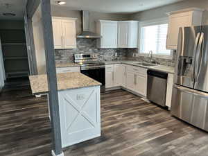 Kitchen with stainless steel appliances, wall chimney exhaust hood, light stone countertops, white cabinets, and tasteful backsplash