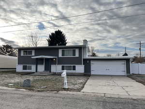 Raised ranch featuring driveway, a garage, a chimney, and brick siding